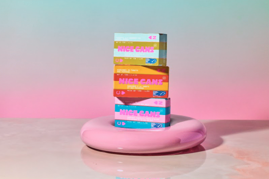 A stack of colourful boxes containing Nice Cans tinned sardines. The cans are stacked inside a pink ring that looks like a floating lifesaver. 